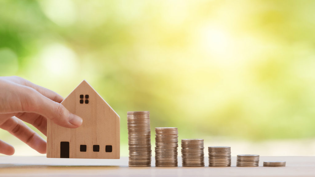 Photographie d'une maquette en bois d'une maison avec des pièces de monnaie en lien avec investissement immobilier. 